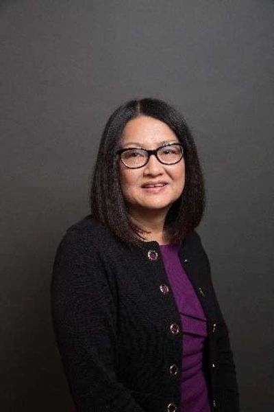 Portrait of a woman with glasses against a dark background.