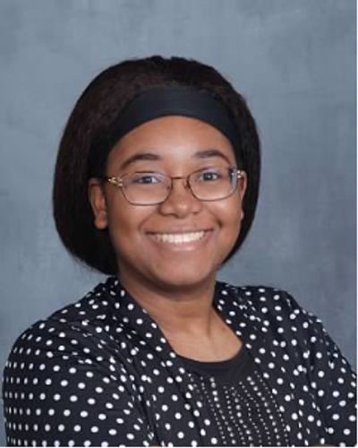 Smiling young woman wearing glasses and a polka dot jacket.