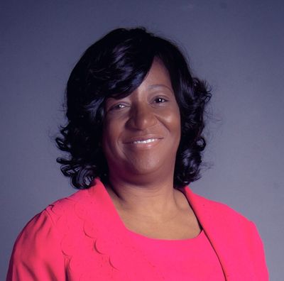A smiling woman with curly black hair wearing a bright pink outfit against a gray background.