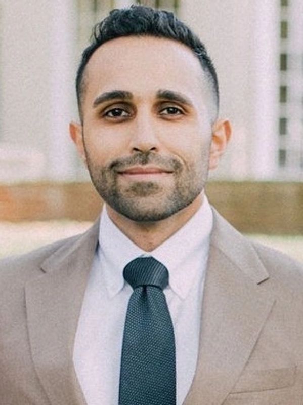 Portrait of a confident man in a beige suit and dark tie.