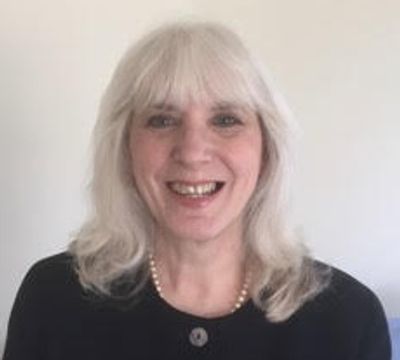 Smiling woman with white hair wearing a black top and pearl necklace.