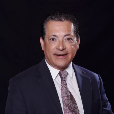 Professional man in suit and patterned tie against black background.