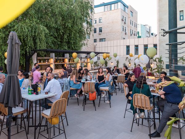 People socializing at an outdoor rooftop party with balloons and drinks.