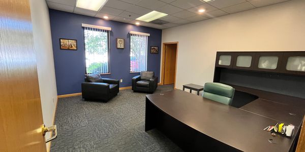 A spacious office with two armchairs and a large desk.