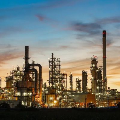 An illuminated industrial refinery complex at dusk under a colorful sky.