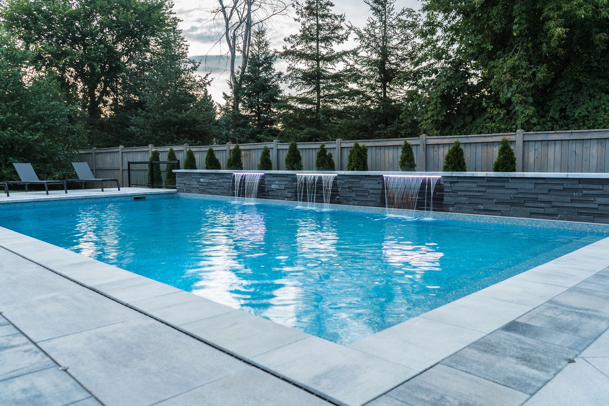 Modern backyard pool with waterfall features and lounge chairs.
