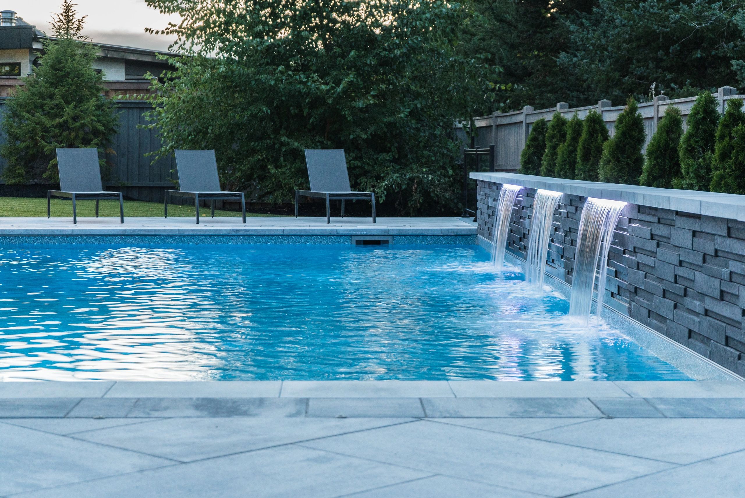 Modern backyard pool with waterfall features and lounge chairs.