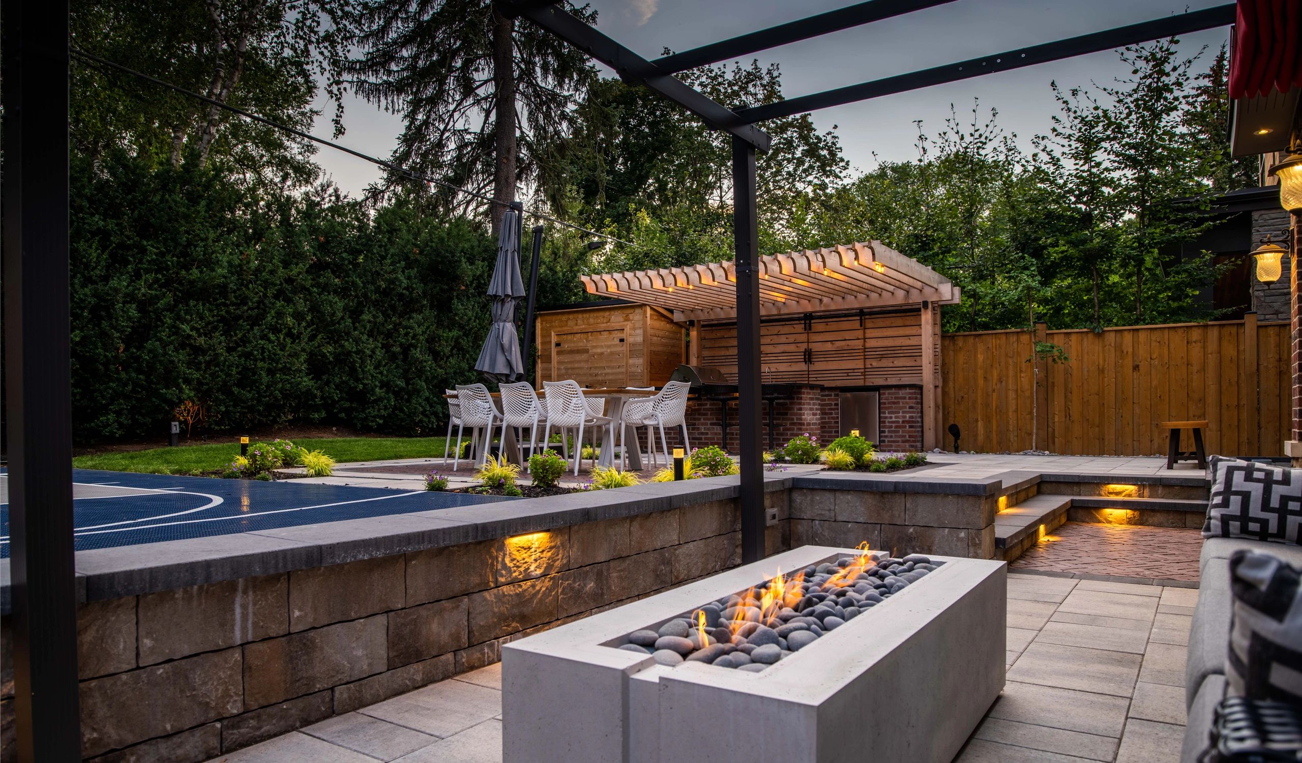Modern backyard with fire pit, dining area, and pergola at dusk.