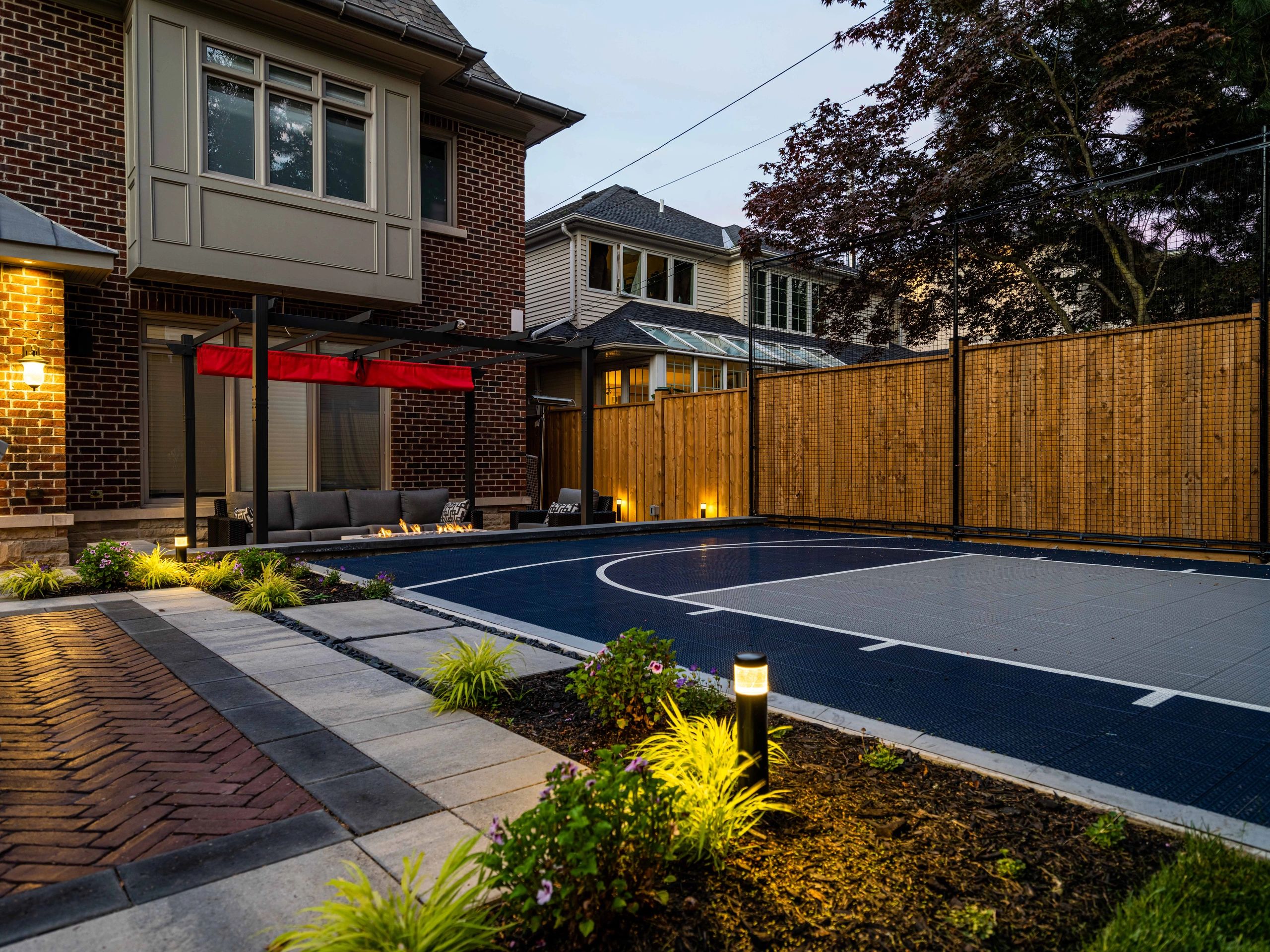 Cozy backyard with a basketball court and seating area illuminated at dusk.