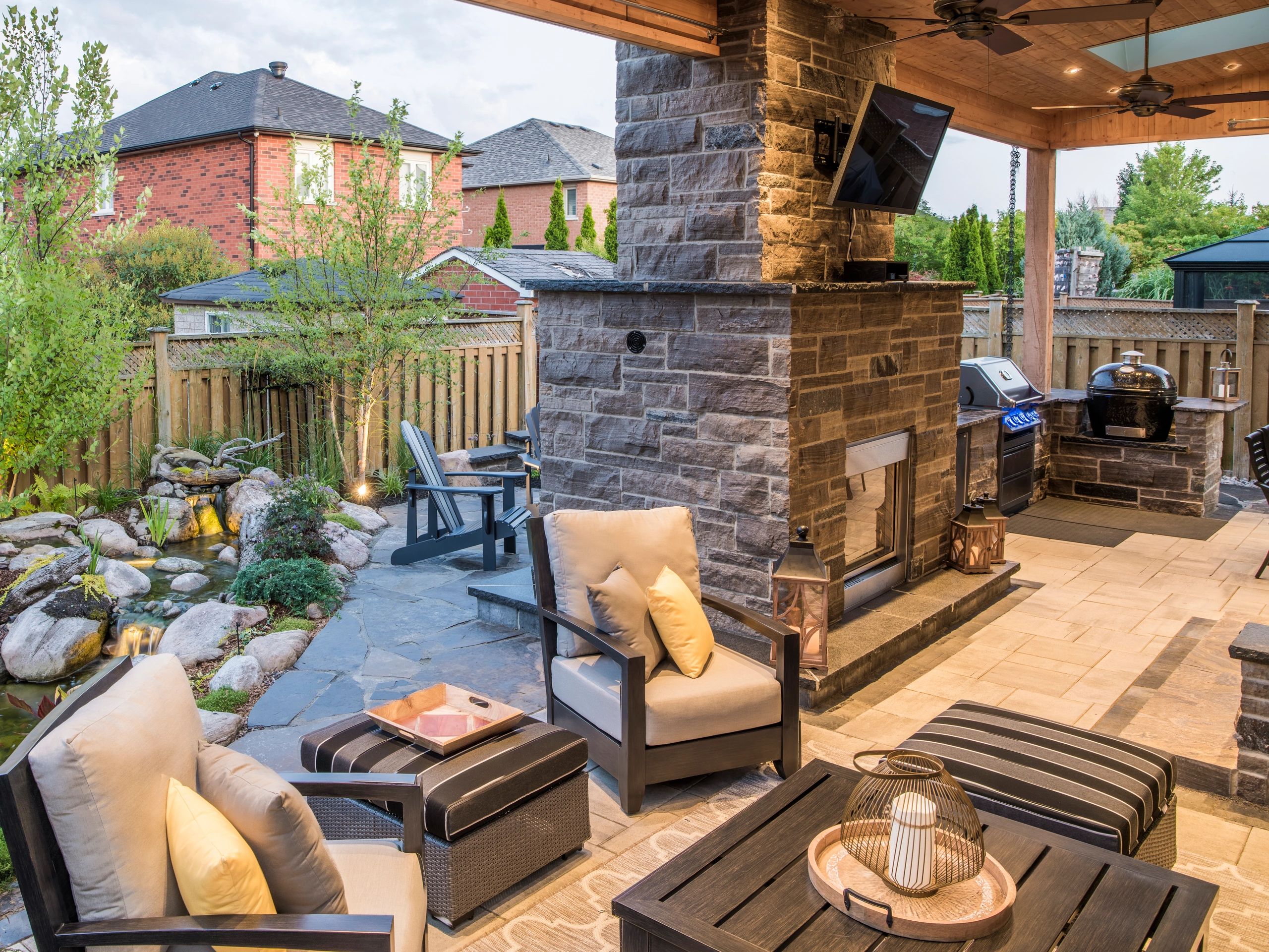 Cozy outdoor patio with seating, fireplace, and BBQ area surrounded by greenery.