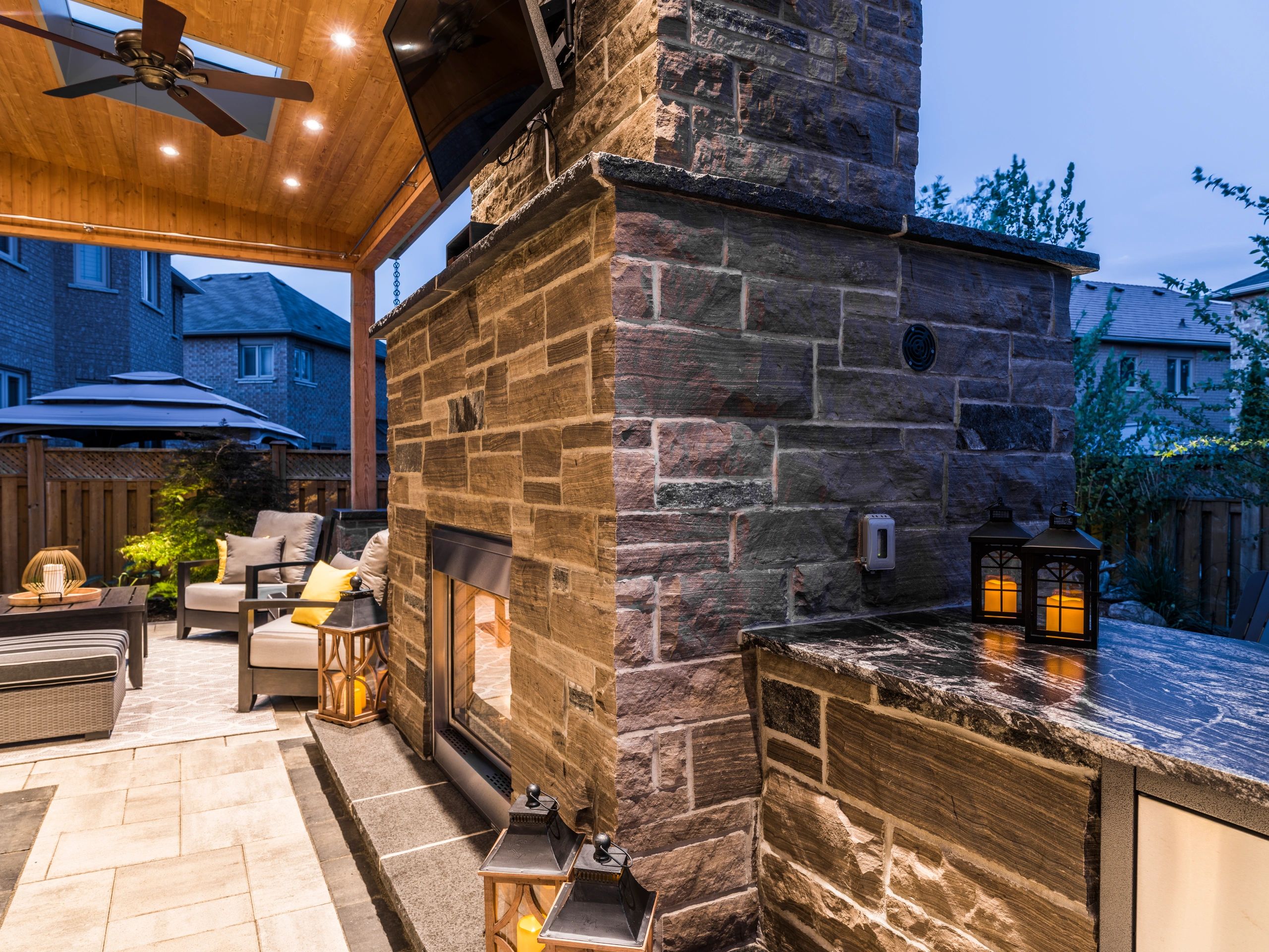 Cozy outdoor patio with stone fireplace and comfortable seating under a wooden ceiling.