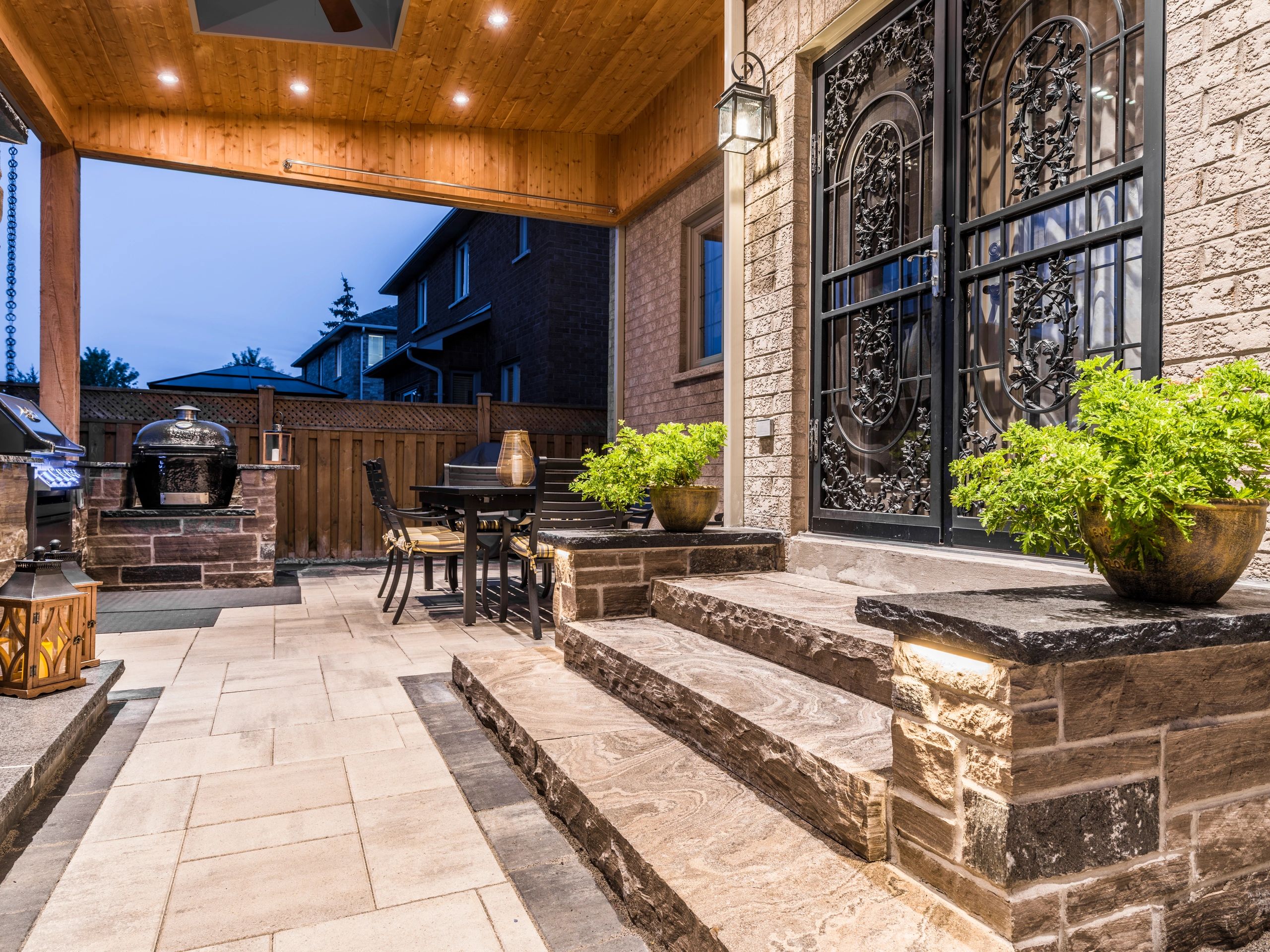 Cozy outdoor patio with stone steps, decorative iron doors, and a dining area under a wooden ceiling.