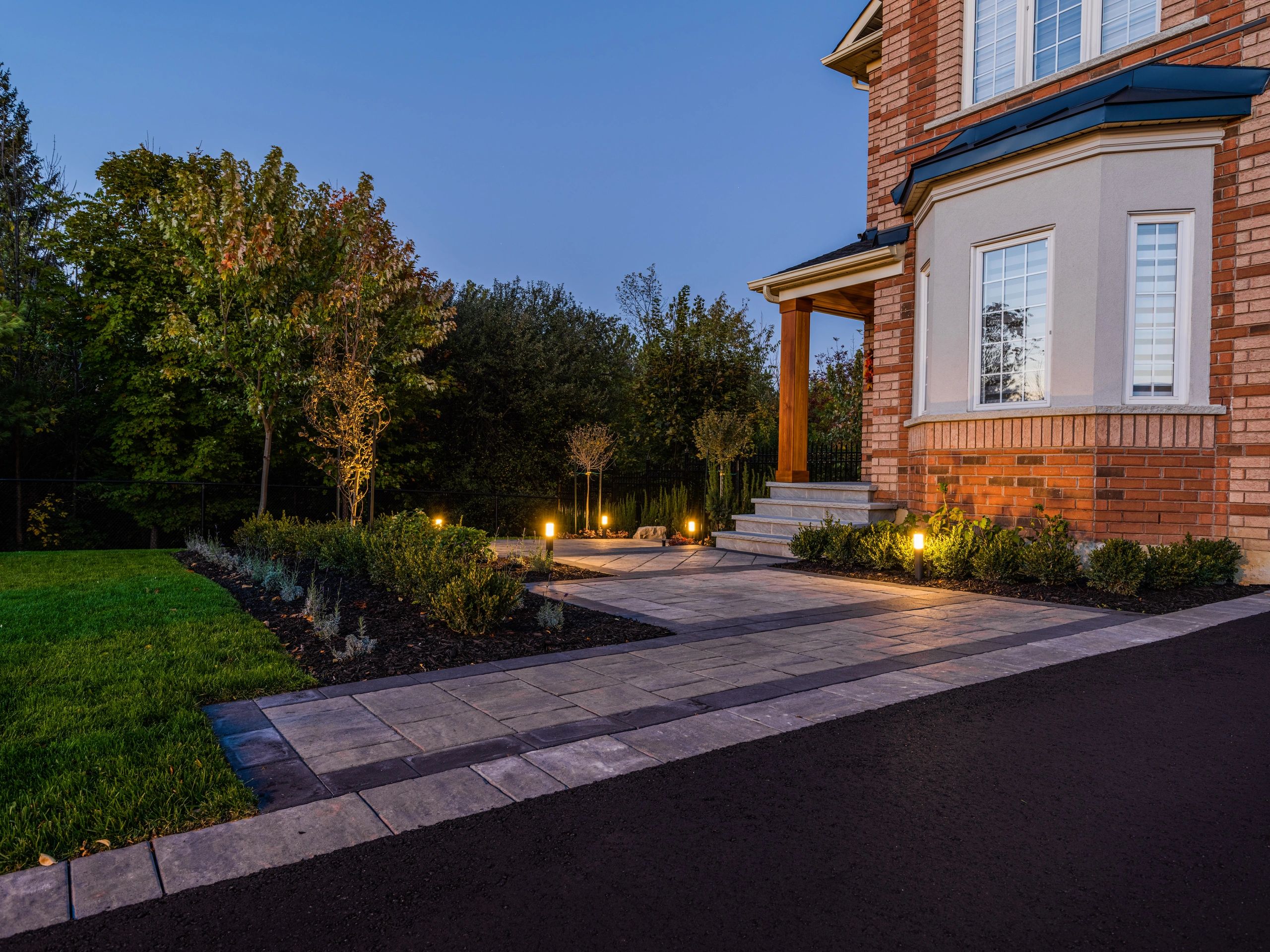 Well-lit walkway and garden in front of a brick house at dusk.