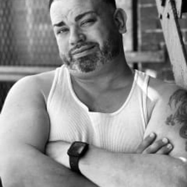 Man in a white tank top with crossed arms and a confident expression.