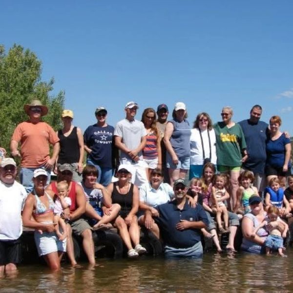 Large group of people, adults and children, posing in shallow water under a clear sky.