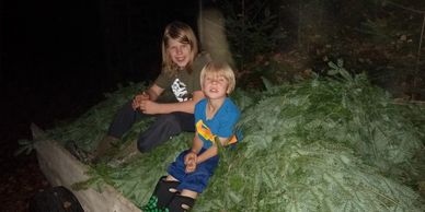 Two children sitting on a pile of greenery in the dark.
