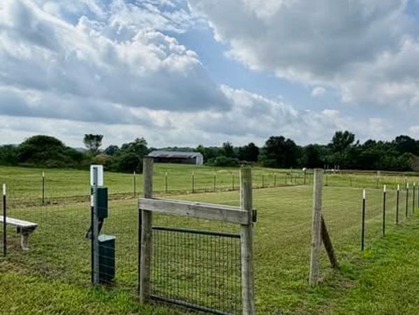 A fenced green field under a cloudy sky with a wooden gate.