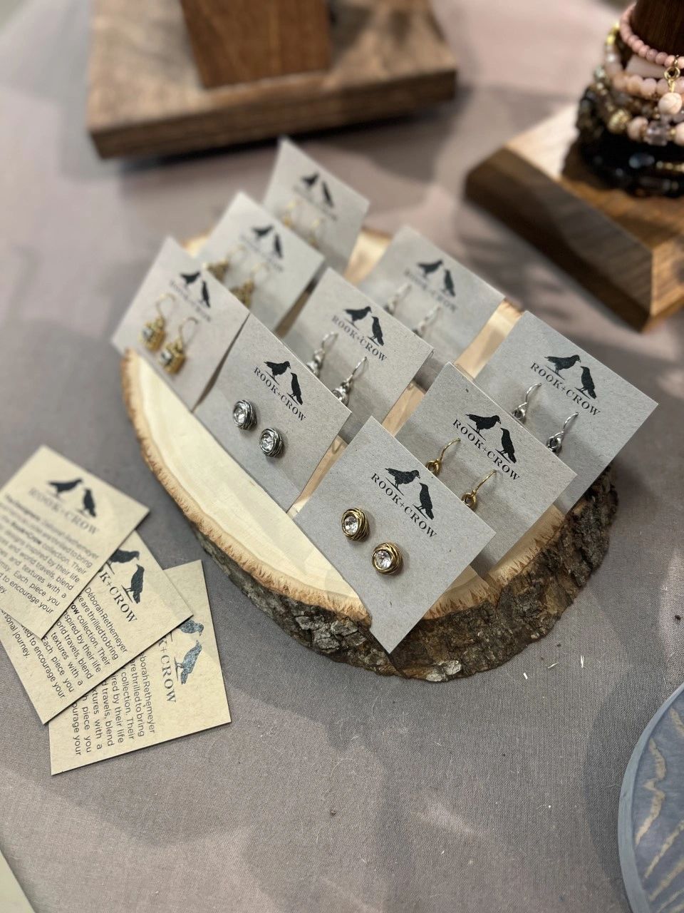 Handcrafted earrings displayed on wood slices with Rook & Crow branding at The Peak in Albertville, MN