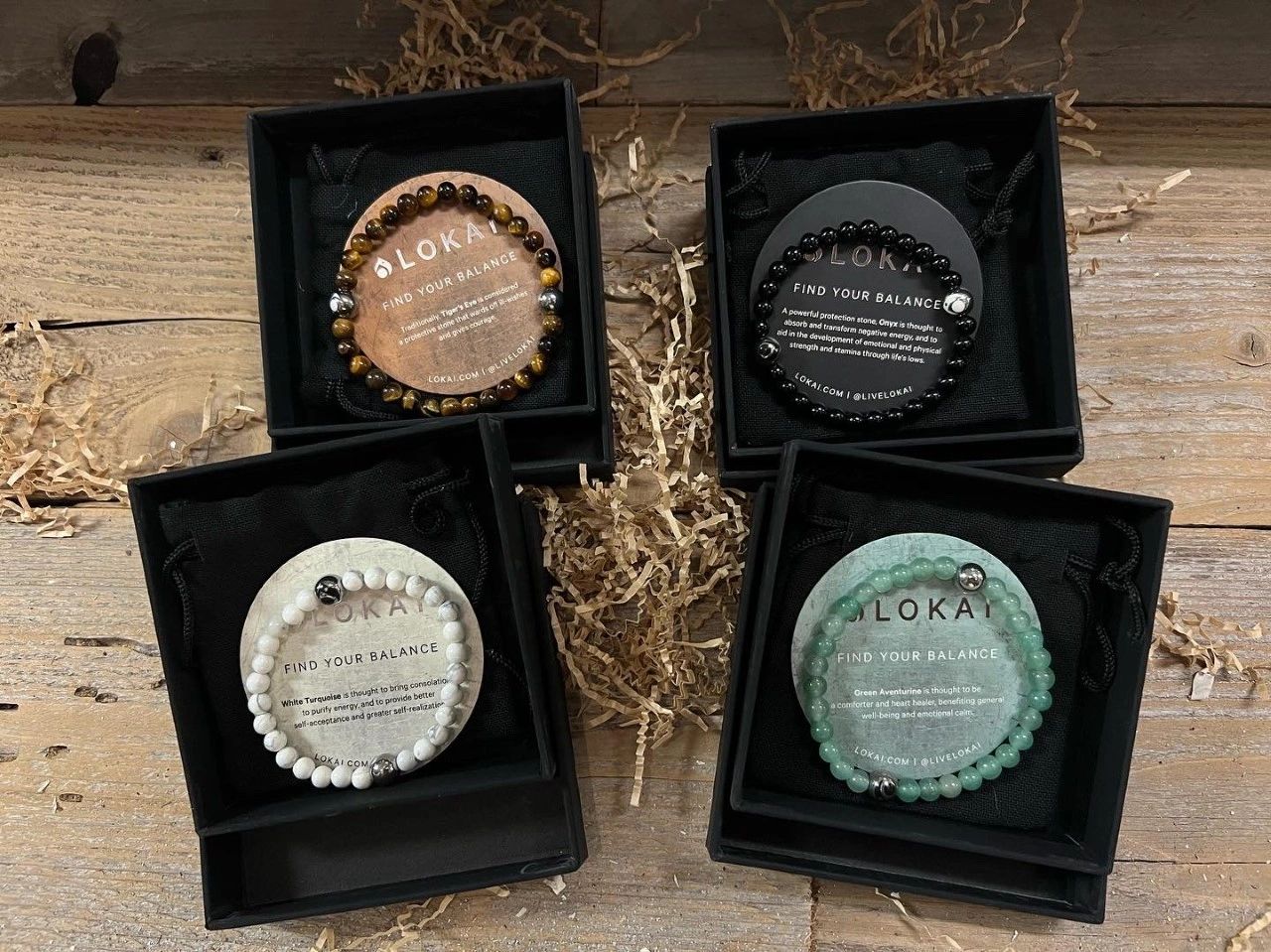 Four Lokai balance bracelets in black boxes on wooden surface at The Peak in Albertville, MN