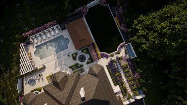 Aerial view of a luxurious backyard with pool, hot tub, and garden surrounded by greenery.