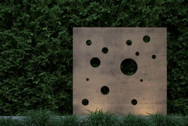 Concrete panel with circular cutouts against lush green foliage.