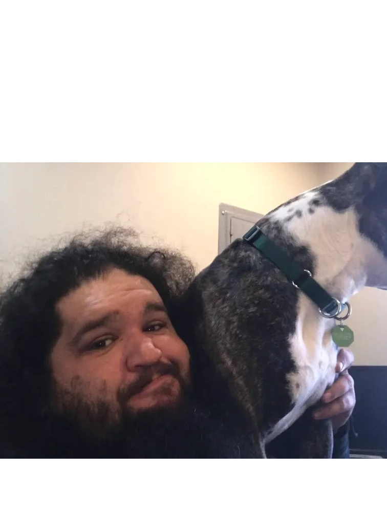 Image shows Farmer sitting on a sofa facing the camera, next to a black and white dog.