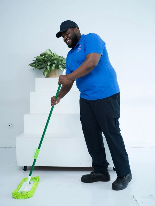 Man in blue shirt happily mopping a white floor indoors.