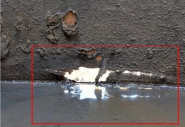 Damaged asphalt with exposed underlying layer and water pooling.