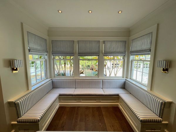Cozy window nook with striped cushions and blinds in a bright room.