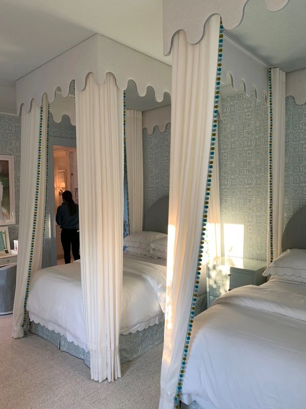 Elegant bedroom with twin canopy beds and delicate blue patterned wallpaper.