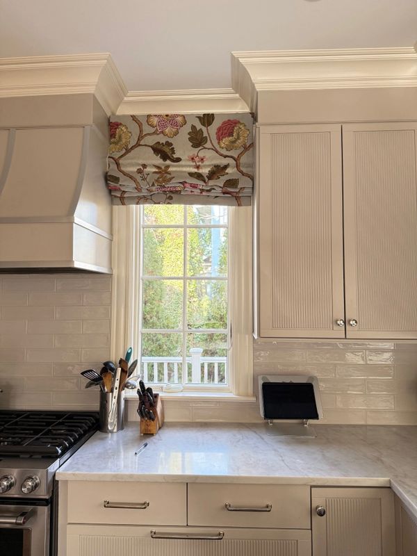Bright kitchen countertop with stove, knife block, and floral window shade.
