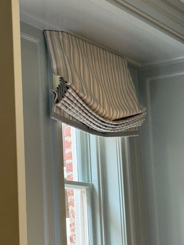 Striped Roman shade partially covering a window with light blue trim.