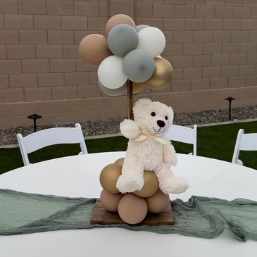 Teddy bear centerpiece with balloons on a table.