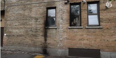 Black scorch marks on a brick wall beneath three windows of a building.
