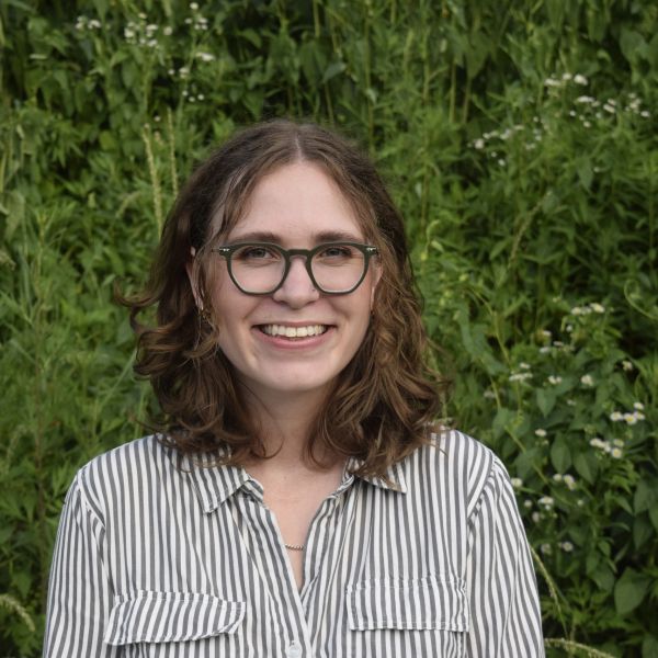 Smiling woman with glasses and curly hair outdoors.