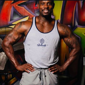 Muscular man in a tank top posing confidently in a vibrant gym.