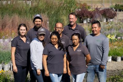Group of eight people posing outdoors in a garden center.