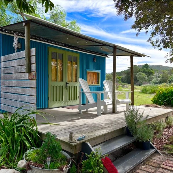 Cozy blue cabin with green doors and white chairs on a wooden porch.