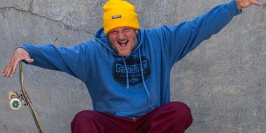Man in colorful outfit posing with skateboard against cracked concrete wall.