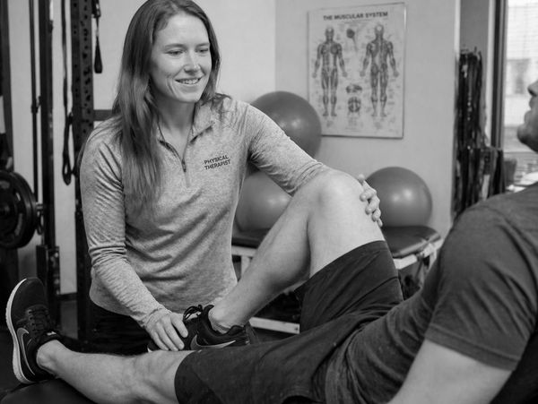Physical therapist assisting a patient with leg exercises in a clinic.