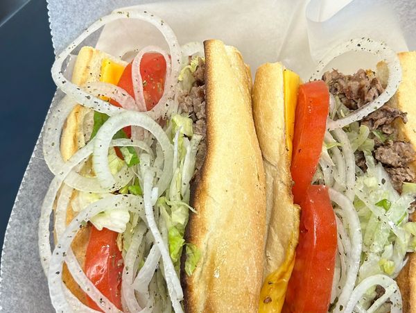 Two hearty sandwiches with onions, tomatoes, lettuce, cheese, and meat on toasted buns.