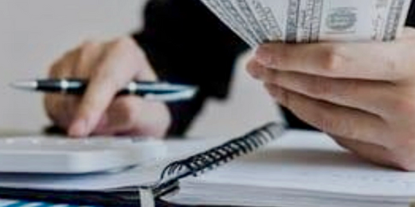 Person holding dollar bills and using a calculator with financial documents nearby.