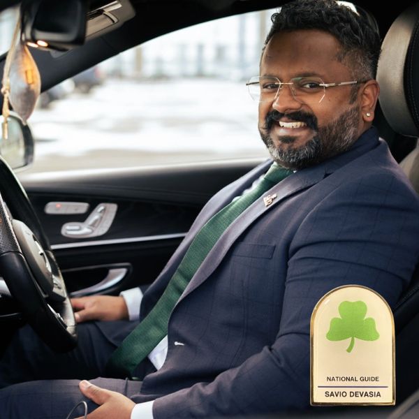 Smiling man in a suit sitting inside a car with a name badge.