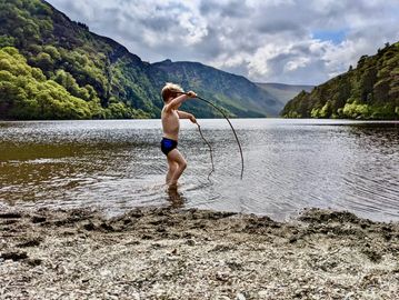 A child playing with sticks in a lake surrounded by mountains.