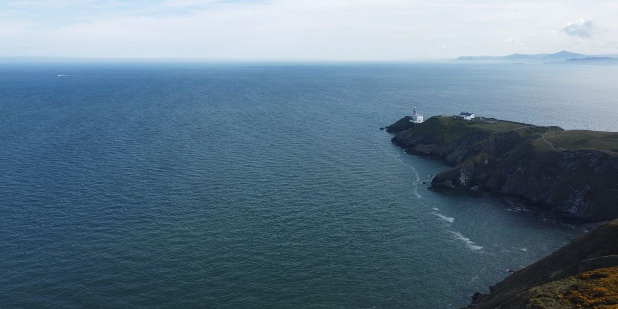 Lighthouse on a rocky coastline overlooking a vast ocean under a clear sky.