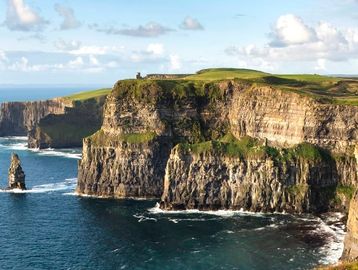 Dramatic cliffs overlooking the ocean under a partly cloudy sky.