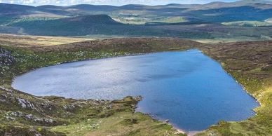 A serene lake nestled among rolling hills under a clear sky.