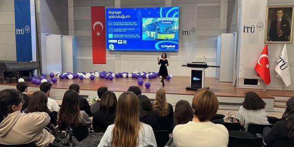 Speaker presenting on career path at İTÜ with audience seated and Turkish flags displayed.