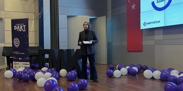 A woman speaking on stage with balloons and a Turkish flag in the background.