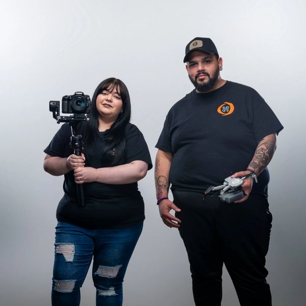 Two individuals holding a camera and a drone in a studio setting.